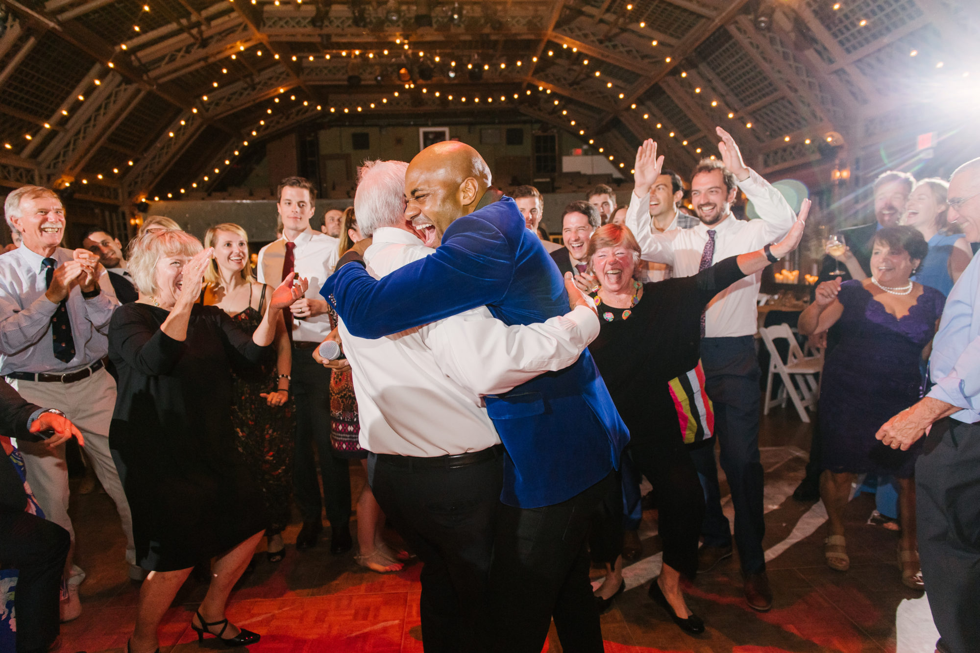 Wedding Photography Tips: How to Take Gorgeous Indoor Wedding Photos by popular New England photographer, Shannon Shipman: image of two men hugging each other while being surrounded by a lot of people. 
