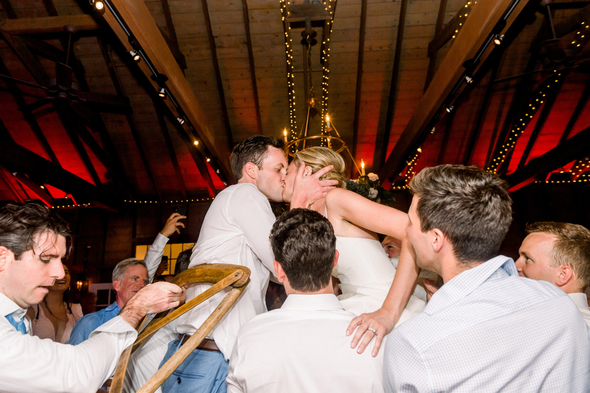 Wedding Photography Tips: How to Take Gorgeous Indoor Wedding Photos by popular New England photographer, Shannon Shipman: image of a bride and groom kissing each other while their surrounded by their wedding party. 