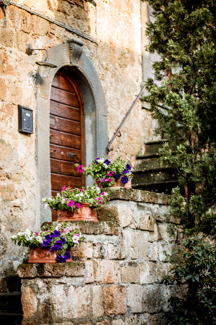 Tuscany Garden Ideas by popular New England travel blogger, Shannon Shipman: image of terracotta pots filled with pink, white, and purple flowers on top of a stone wall. 