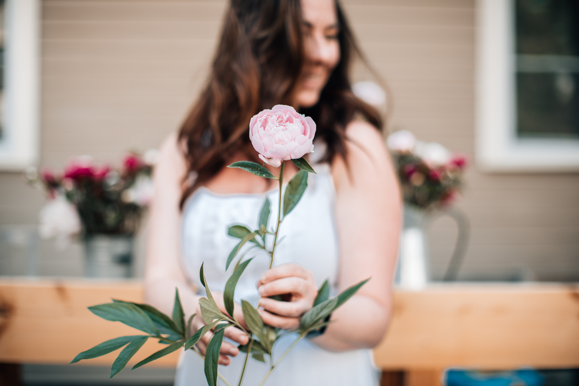 Caring for Peonies by popular New England blogger, Shannon Shipman: image of Shannon Shipman wearing a white dress and holding a light pink peony. 