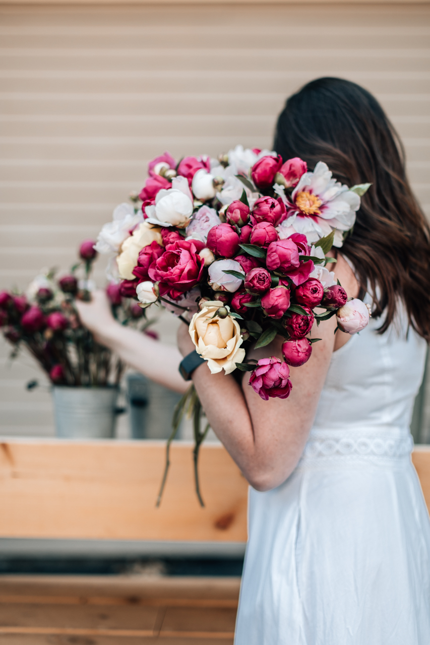 How to Harvest Peonies, and Make Them Last All Summer! | Caring for Peonies by popular New England blogger, Shannon Shipman: image of Shannon Shipman wearing a white dress and holding a bouquet of pink and white peonies. 
